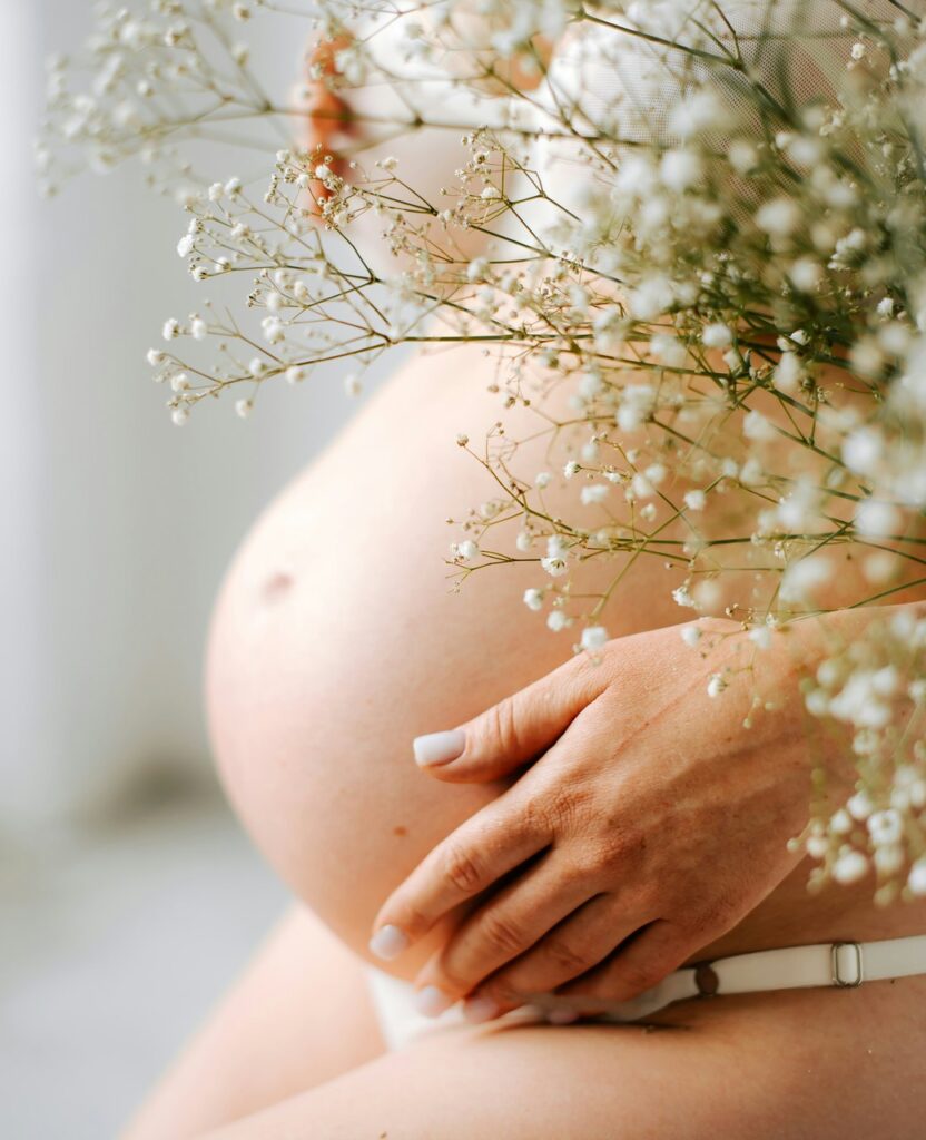 Schwangere hält ihren Babybauch, umgeben von Schleierkraut